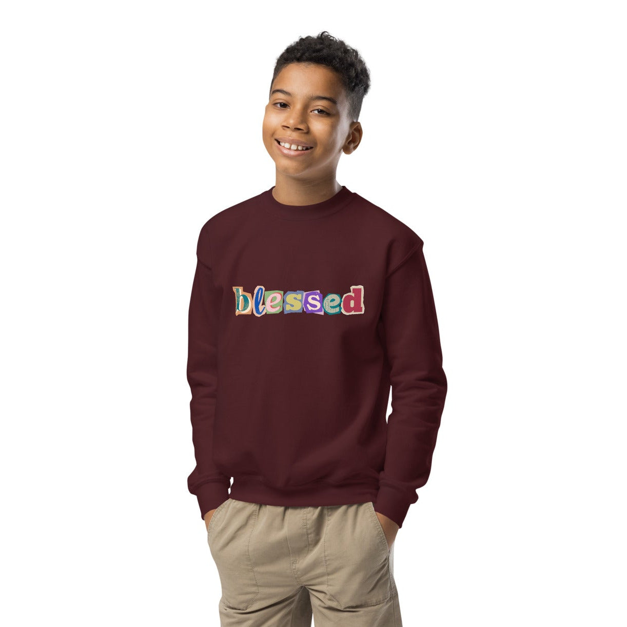 Child wearing a maroon sweatshirt with 'blessed' text, beige shorts, and white shoes on a white background
